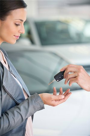 Side profile of a young woman taking car key in showroom Stock Photo - Premium Royalty-Free, Code: 6108-05871424