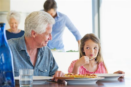 simsearch:6108-05871546,k - Fille de manger de la nourriture à une table à manger avec son grand-père, assis près d'elle Photographie de stock - Premium Libres de Droits, Code: 6108-05871544