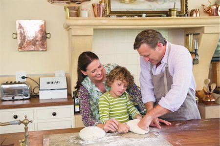 Cute little boy and his parents kneading dough at kitchen Stock Photo - Premium Royalty-Free, Code: 6108-05871804