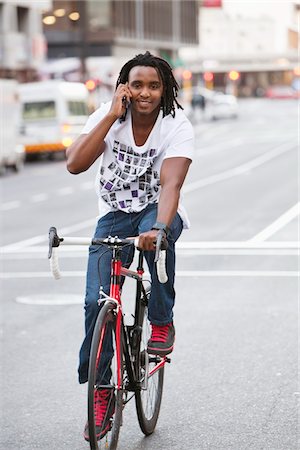 Smiling man talking on a mobile phone while riding a bicycle Stock Photo - Premium Royalty-Free, Code: 6108-05872132