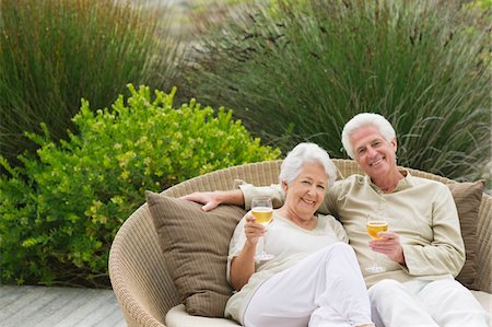 Senior couple sitting in a wicker couch holding wine glasses Stock Photo - Premium Royalty-Free, Code: 6108-05872396