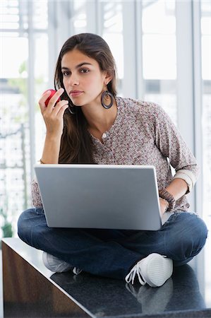Beautiful woman eating an apple while using a laptop Stock Photo - Premium Royalty-Free, Code: 6108-05872329