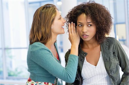 people gossiping - Side profile of a woman whispering in her friend's ear in university Stock Photo - Premium Royalty-Free, Code: 6108-05872339