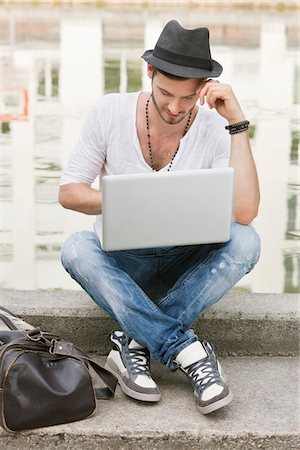 Man sitting on the ledge of a canal and using a laptop, Paris, Ile-de-France, France Stock Photo - Premium Royalty-Free, Code: 6108-05872879