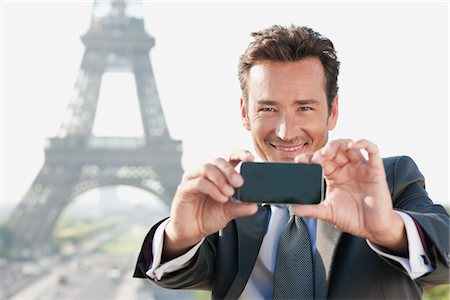 Businessman taking a picture with a mobile phone with the Eiffel Tower in the background, Paris, Ile-de-France, France Stock Photo - Premium Royalty-Free, Code: 6108-05872892