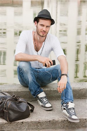 Man sitting on the ledge of a canal and listening to music with an MP3 player, Paris, Ile-de-France, France Stock Photo - Premium Royalty-Free, Code: 6108-05873013