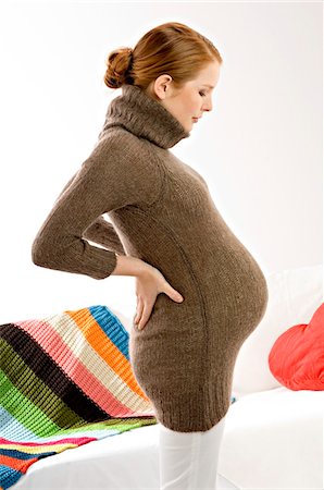 pregnancy - Side profile of a pregnant young woman standing and looking at her abdomen Stock Photo - Premium Royalty-Free, Code: 6108-05873628