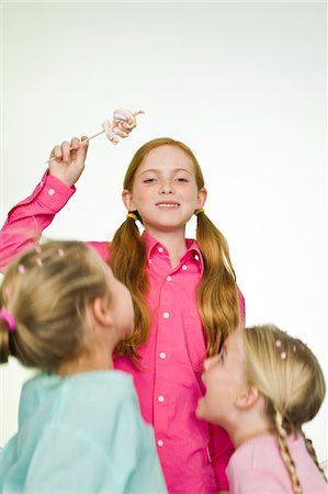 Girl holding a lollipop with her two friends standing beside her Stock Photo - Premium Royalty-Free, Code: 6108-05874081