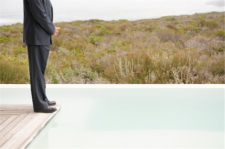 Low section view of a businessman standing on a platform at an infinity pool Stock Photo - Premium Royalty-Free, Code: 6108-05874254