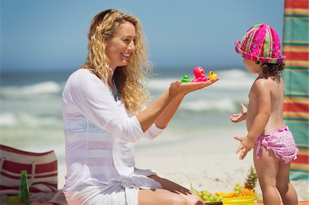 parent kneeling - Woman giving toys to her daughter on the beach Stock Photo - Premium Royalty-Free, Code: 6108-05874975