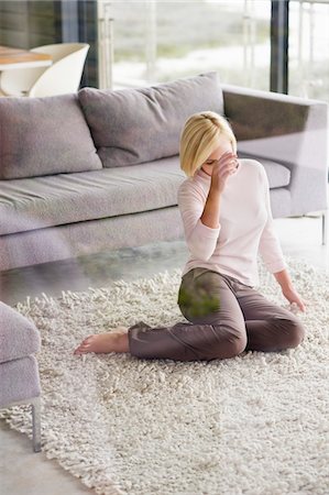 Young woman sitting on a rug and thinking Stock Photo - Premium Royalty-Free, Code: 6108-05874922