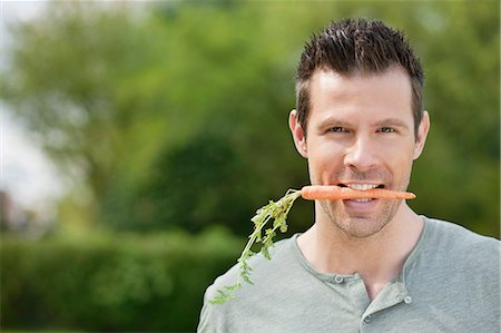 Man holding a carrot in his mouth Stock Photo - Premium Royalty-Free, Code: 6108-06166672