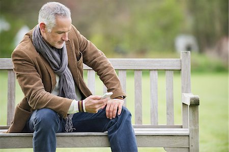 Man text messaging on a mobile phone in a park Stock Photo - Premium Royalty-Free, Code: 6108-06166914