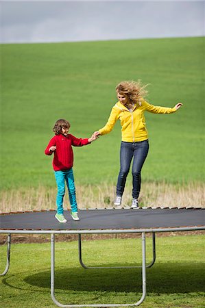 Woman with her son jumping on a trampoline in a field Stock Photo - Premium Royalty-Free, Code: 6108-06167352