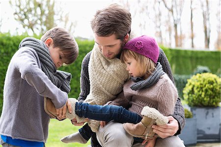 dress up girl - Boy putting shoe on his sister sitting in her father's lap Stock Photo - Premium Royalty-Free, Code: 6108-06167574