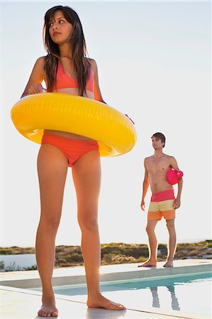 Woman walking with inflatable ring at the poolside with a man behind her Stock Photo - Premium Royalty-Free, Code: 6108-06904681