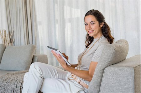simsearch:6108-06904945,k - Beautiful woman using a digital tablet and smiling on a couch Stock Photo - Premium Royalty-Free, Code: 6108-06904843