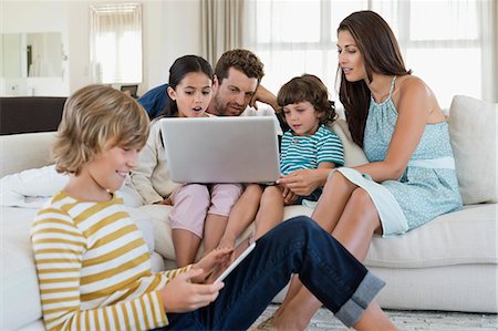 Family using electronic gadgets in a living room Stock Photo - Premium Royalty-Free, Code: 6108-06904844