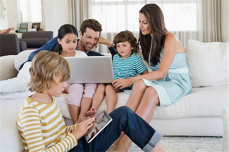 five - Boy using a digital tablet with his family looking at a laptop Stock Photo - Premium Royalty-Free, Code: 6108-06904857