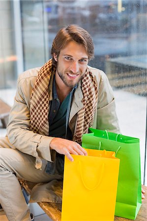 Portrait of a smiling man sitting at an airport lounge with shopping bags Stock Photo - Premium Royalty-Free, Code: 6108-06904930