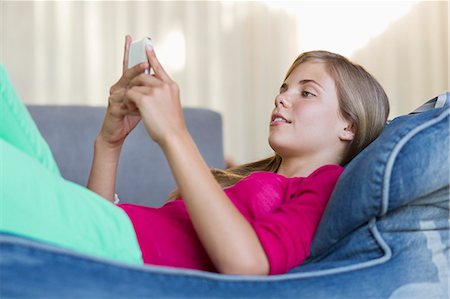 Girl lying on a bean bag and using a mobile phone Stock Photo - Premium Royalty-Free, Code: 6108-06905259