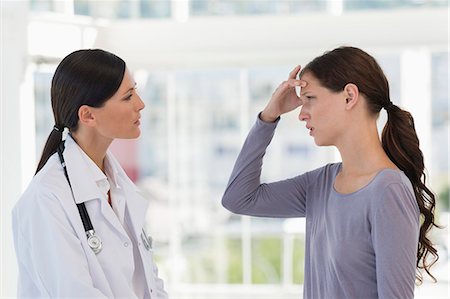 Female patient gesturing headache while discussing with a doctor Foto de stock - Sin royalties Premium, Código: 6108-06905664