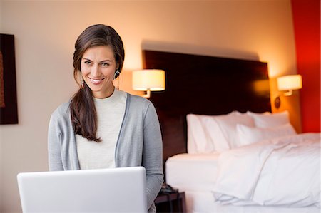 Woman using a laptop in a hotel room and smiling Stock Photo - Premium Royalty-Free, Code: 6108-06905976