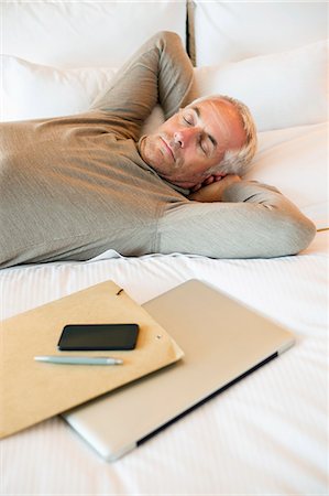 resting on the bed - Man resting on the bed with a laptop and file in a hotel room Stock Photo - Premium Royalty-Free, Code: 6108-06906129