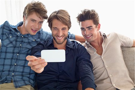 Three friends sitting on a couch and looking at mobile phone Stock Photo - Premium Royalty-Free, Code: 6108-06907329