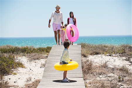 Children with their parents holding inflatable rings on a boardwalk on the beach Foto de stock - Sin royalties Premium, Código: 6108-06907544