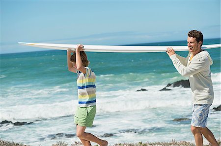 Man and his son carrying a surfboard on the beach Stock Photo - Premium Royalty-Free, Code: 6108-06907589