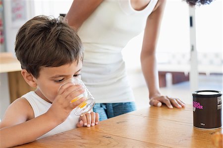family dining room table - Boy drinking orange juice with his mother standing behind him Stock Photo - Premium Royalty-Free, Code: 6108-06907711