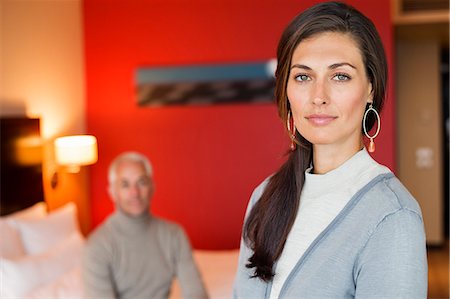 Portrait of a woman in a hotel room with her husband in the background Stock Photo - Premium Royalty-Free, Code: 6108-06907853
