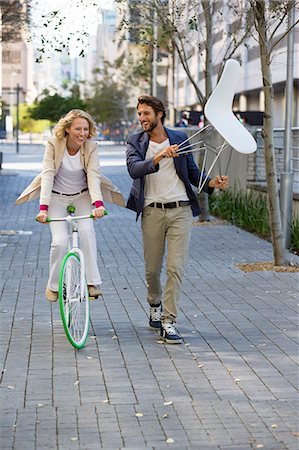 people walking in the street - Woman riding a bicycle with a man carrying a chair beside her Stock Photo - Premium Royalty-Free, Code: 6108-06908148