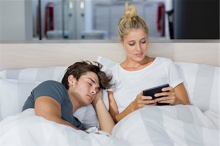 simsearch:649-01696405,k - Young woman using a digital tablet with her boyfriend sleeping near her Stock Photo - Premium Royalty-Free, Code: 6108-08662536