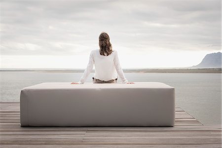 Rear view of a woman sitting on ottoman at lakeshore Stock Photo - Premium Royalty-Free, Code: 6108-08663428