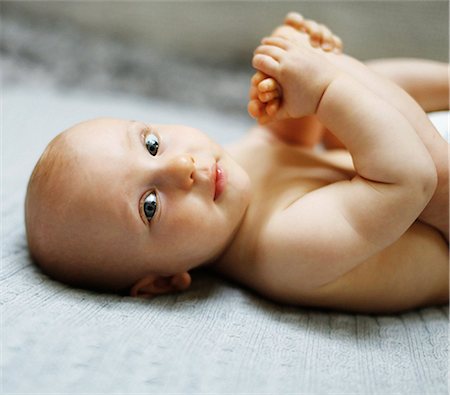 8 months baby boy lying down and playing with his feet Stock Photo - Premium Royalty-Free, Code: 6108-08636835