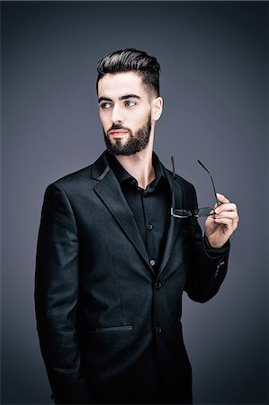 Portrait of a young businessman holding a pair of glasses, the look on the side Stock Photo - Premium Royalty-Free, Code: 6108-08637415