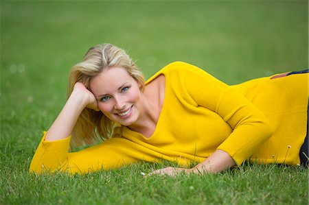 Portrait of a pretty blond woman lying down in the park smiling at camera Fotografie stock - Premium Royalty-Free, Codice: 6108-08943406