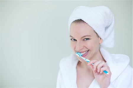Woman in bathrobe brushing her teeth and smiling at camera Stock Photo - Premium Royalty-Free, Code: 6108-08943570