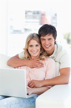 A man and woman embrace as they use the laptop and look forward. Stock Photo - Premium Royalty-Free, Code: 6109-06003167
