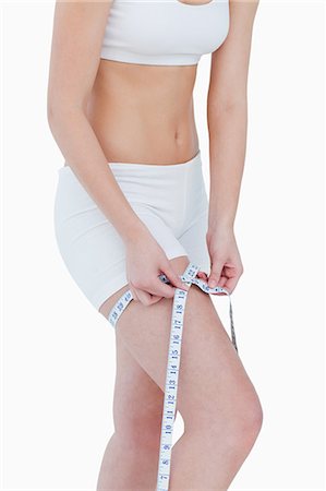 Young woman using a measure tape for her thigh against a white background Stock Photo - Premium Royalty-Free, Code: 6109-06003361