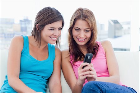 people gossiping - Teenagers sitting side by side on the sofa while looking at a cellphone Stock Photo - Premium Royalty-Free, Code: 6109-06003317