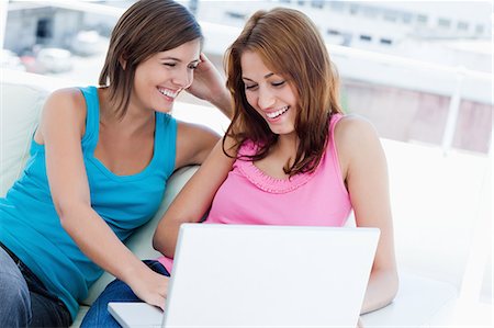 Young woman holding a laptop accompanied by her friend sitting on a white sofa Stock Photo - Premium Royalty-Free, Code: 6109-06003327