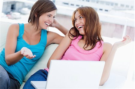 Two smiling friends talking about the laptop while sitting on a sofa Stock Photo - Premium Royalty-Free, Code: 6109-06003329