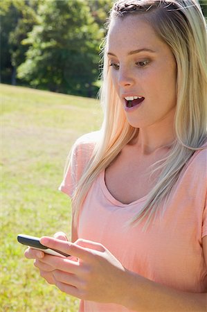 Young attractive blonde girl showing her surprise while receiving a text in a parkland Stock Photo - Premium Royalty-Free, Code: 6109-06003564