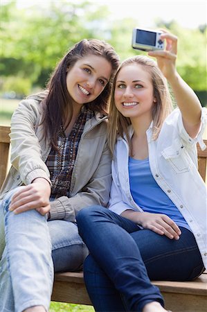 Young woman taking a picture of herself and her friend while sitting on a bench Stock Photo - Premium Royalty-Free, Code: 6109-06003518