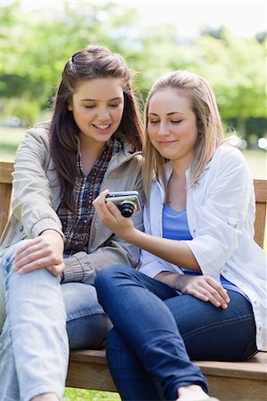 Young smiling girls looking at the digital camera while sitting on a bench in a park Stock Photo - Premium Royalty-Free, Code: 6109-06003519