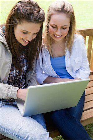 Young smiling teenagers looking at a laptop while sitting on a bench in a parkland Stock Photo - Premium Royalty-Free, Code: 6109-06003523