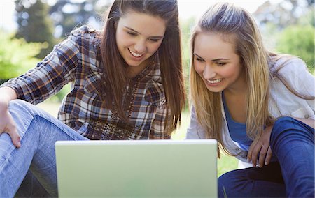 Young happy girls attentively looking at a laptop while sitting on the grass in a park Stock Photo - Premium Royalty-Free, Code: 6109-06003528